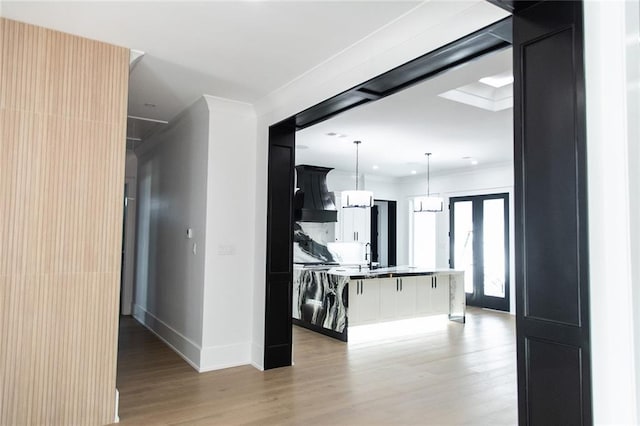 kitchen featuring a kitchen island with sink, dark cabinets, crown molding, light wood-style floors, and pendant lighting