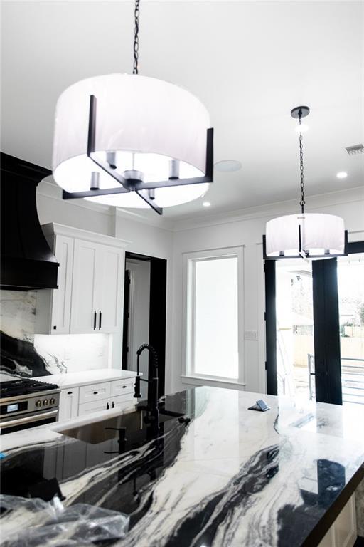 kitchen with visible vents, white cabinets, light stone counters, crown molding, and premium range hood