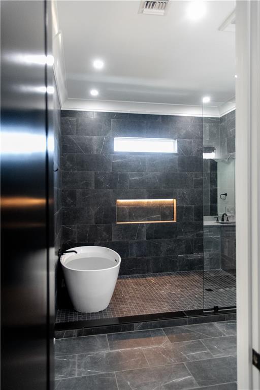 full bath with ornamental molding, a stall shower, visible vents, and tile walls