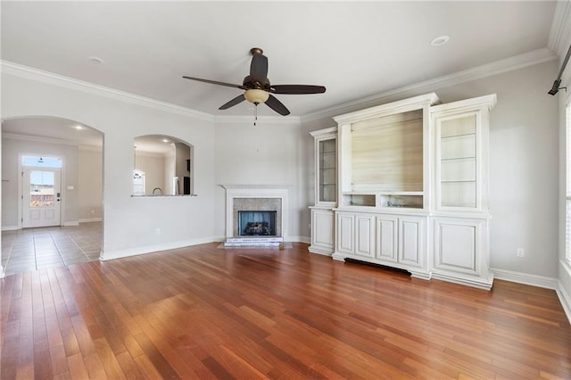 unfurnished living room featuring hardwood / wood-style flooring, baseboards, a fireplace with raised hearth, and crown molding