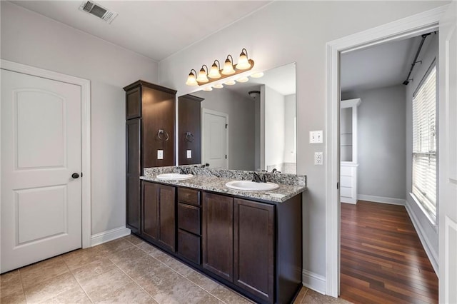 bathroom with double vanity, baseboards, visible vents, and a sink