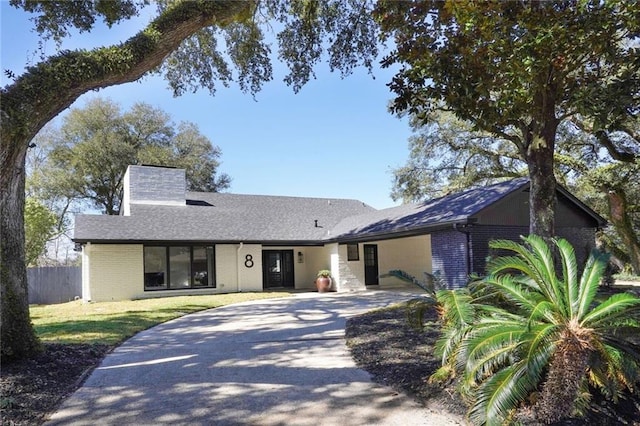 ranch-style house featuring concrete driveway, brick siding, fence, and a chimney