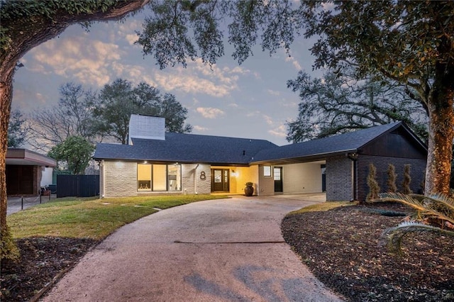 ranch-style house with brick siding, a yard, a chimney, concrete driveway, and fence