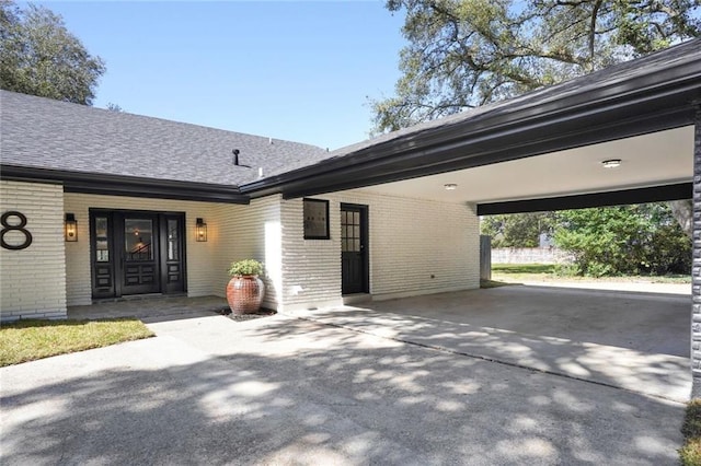 exterior space featuring a carport, roof with shingles, concrete driveway, and brick siding