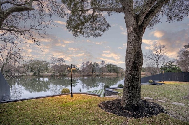 yard at dusk featuring a water view and fence