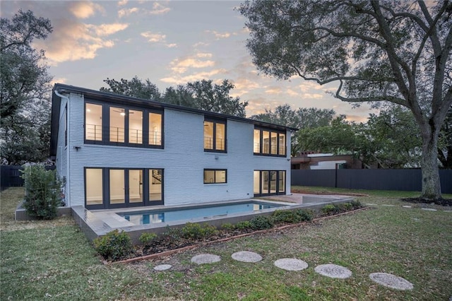 back of house at dusk with a lawn, fence, and a fenced in pool