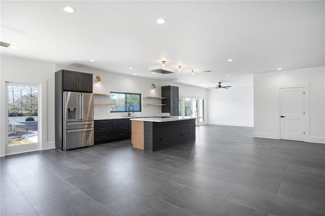 kitchen with high quality fridge, a kitchen island, a sink, light countertops, and open shelves