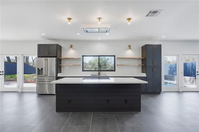 kitchen with a center island, open shelves, high end fridge, light countertops, and visible vents