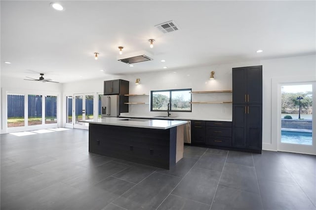 kitchen with a kitchen island, visible vents, light countertops, stainless steel refrigerator with ice dispenser, and open shelves