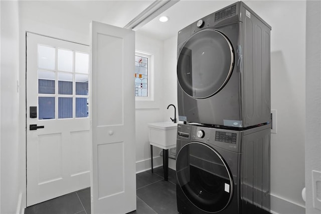 laundry area with recessed lighting, laundry area, dark tile patterned flooring, baseboards, and stacked washing maching and dryer