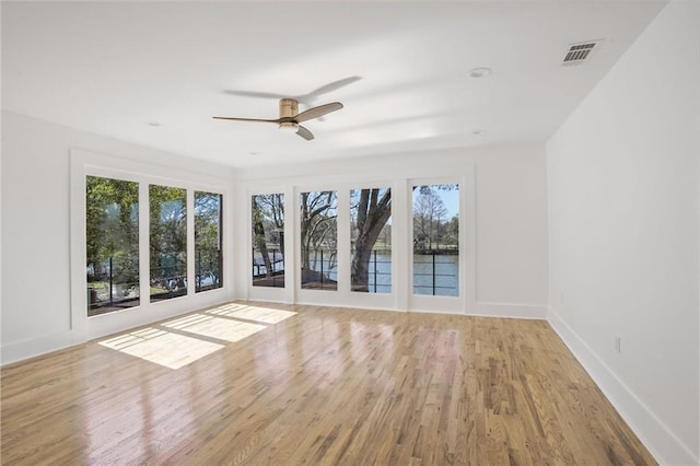 empty room featuring ceiling fan, wood finished floors, visible vents, and baseboards