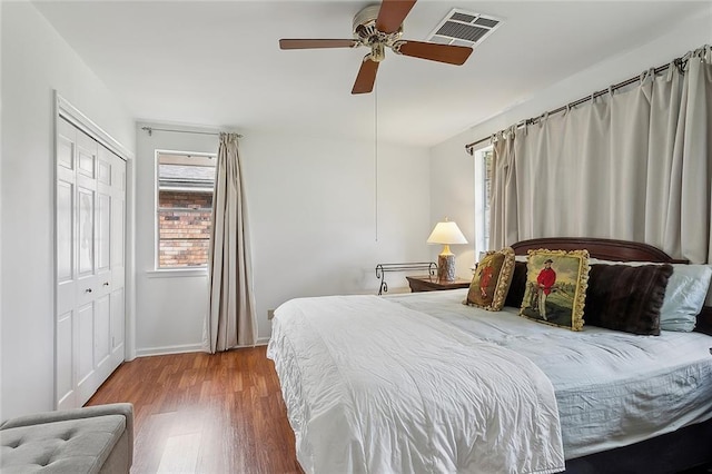 bedroom with ceiling fan, wood finished floors, visible vents, baseboards, and a closet