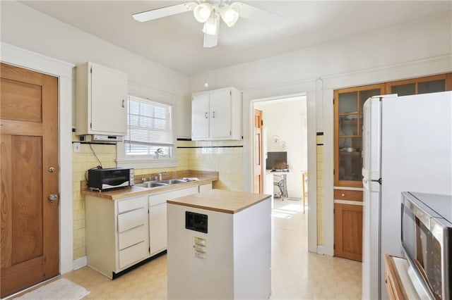 kitchen with a sink, white cabinets, freestanding refrigerator, light floors, and stainless steel microwave