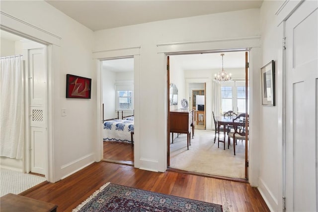 corridor featuring a chandelier, hardwood / wood-style flooring, and baseboards