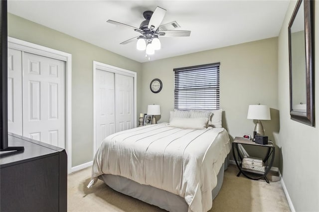 bedroom featuring two closets, light colored carpet, visible vents, ceiling fan, and baseboards