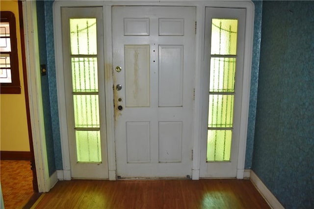 doorway with baseboards, wood finished floors, and wallpapered walls