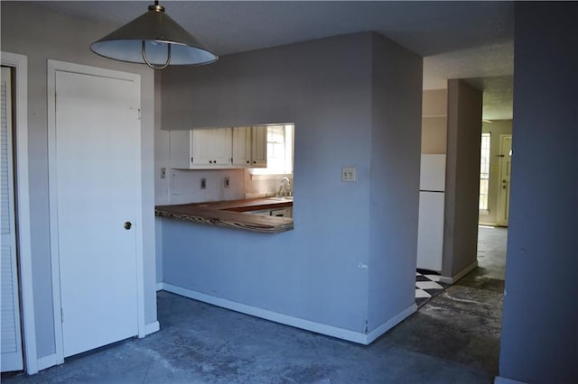 kitchen with unfinished concrete flooring, a sink, freestanding refrigerator, and baseboards