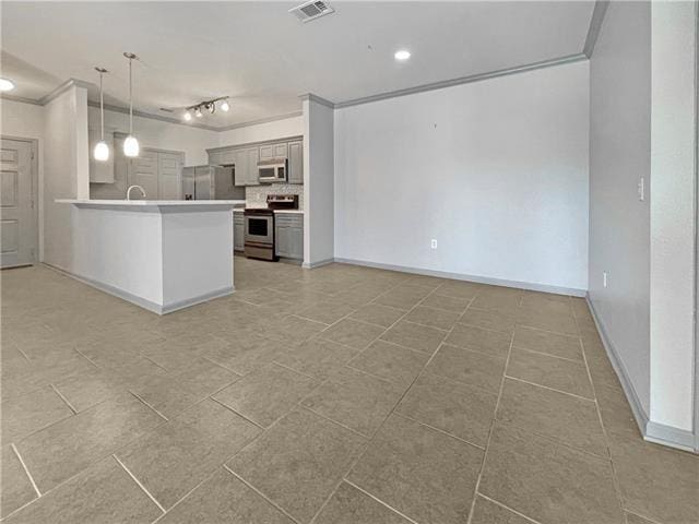 kitchen featuring appliances with stainless steel finishes, open floor plan, ornamental molding, a peninsula, and light countertops