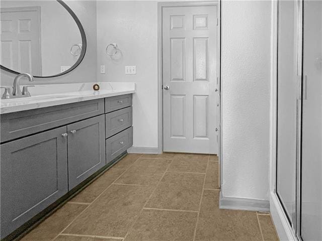 bathroom featuring a shower with door, tile patterned flooring, baseboards, and vanity