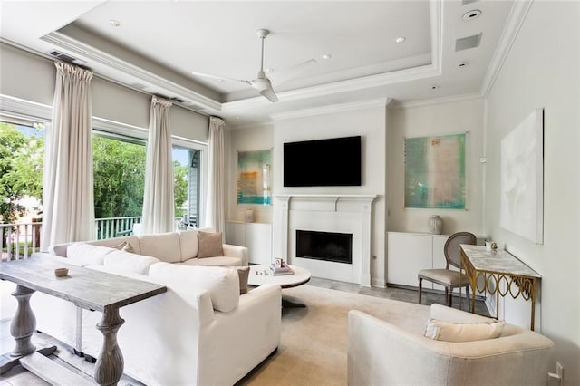 living room with a tray ceiling, crown molding, a fireplace, and ceiling fan