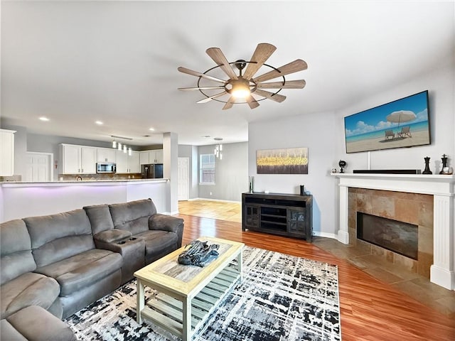 living room featuring a fireplace, recessed lighting, light wood-style flooring, a ceiling fan, and baseboards