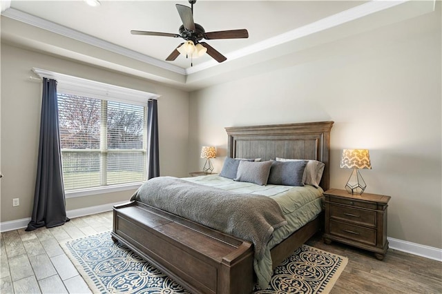 bedroom with ceiling fan, baseboards, ornamental molding, light wood-type flooring, and a raised ceiling