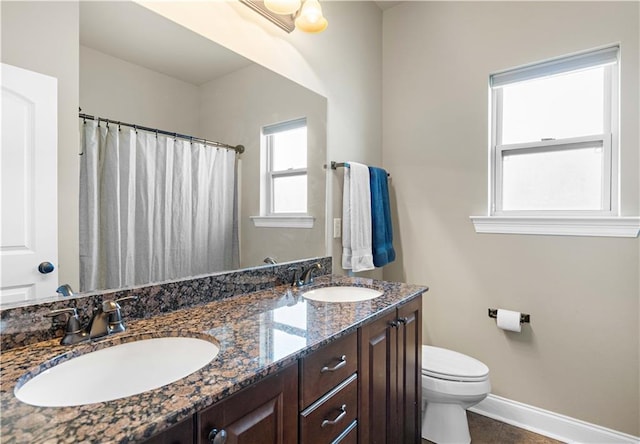 bathroom featuring baseboards, a sink, toilet, and double vanity