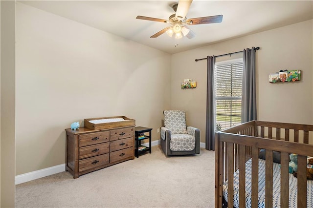 bedroom featuring light carpet, baseboards, a ceiling fan, and a crib