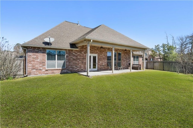 back of property with a fenced backyard, brick siding, a yard, roof with shingles, and a patio area