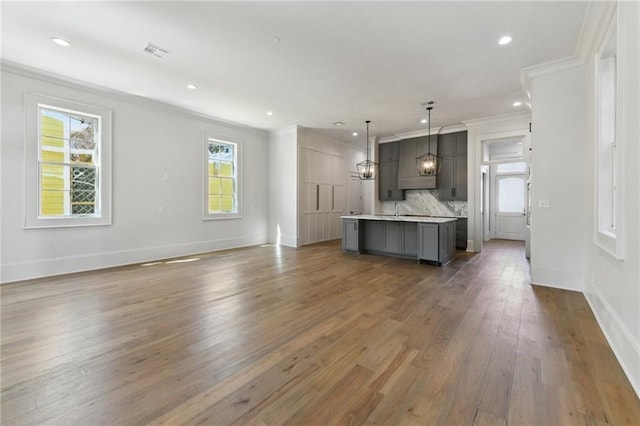 kitchen with visible vents, ornamental molding, open floor plan, wood finished floors, and a kitchen island with sink