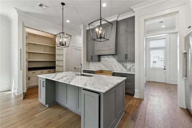 kitchen with visible vents, gray cabinetry, ornamental molding, light wood-style floors, and a sink