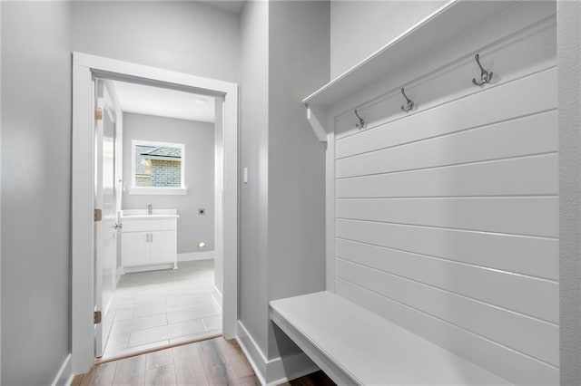 mudroom with light wood finished floors, a sink, and baseboards