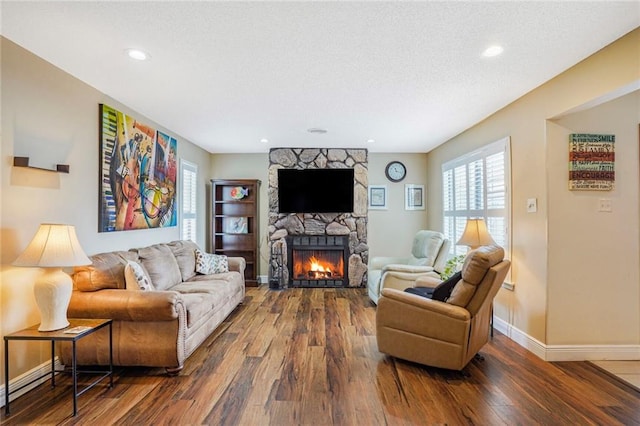 living room featuring baseboards, wood finished floors, a textured ceiling, a stone fireplace, and recessed lighting