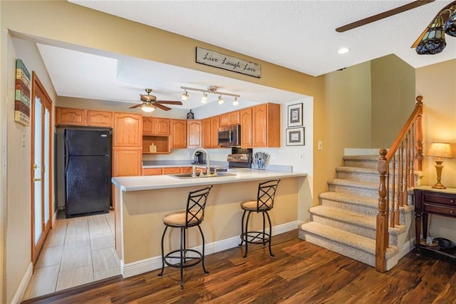 kitchen with a ceiling fan, stainless steel microwave, freestanding refrigerator, a peninsula, and a sink