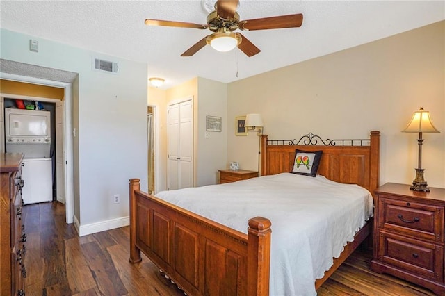 bedroom featuring baseboards, visible vents, dark wood finished floors, a textured ceiling, and stacked washing maching and dryer