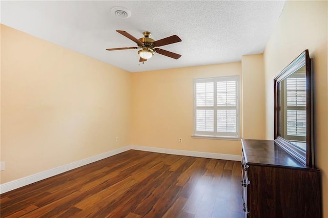 empty room with dark wood finished floors, visible vents, ceiling fan, a textured ceiling, and baseboards