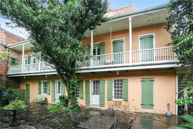 rear view of house with a balcony, a patio, and stucco siding