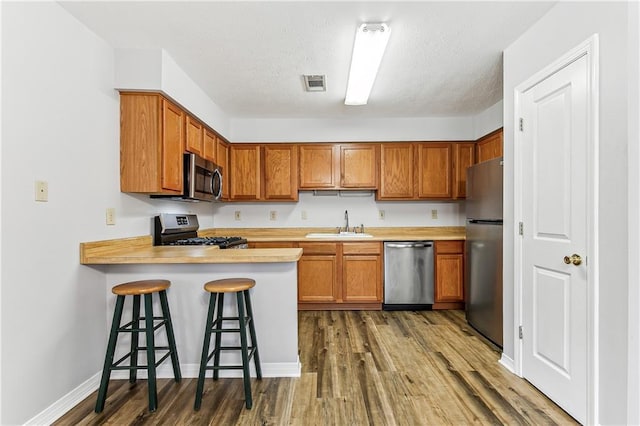 kitchen with visible vents, appliances with stainless steel finishes, a peninsula, light countertops, and a sink