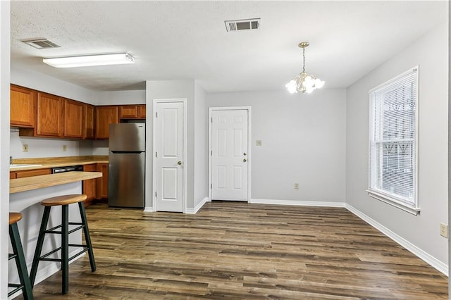 kitchen with dark wood-style floors, freestanding refrigerator, brown cabinetry, and visible vents