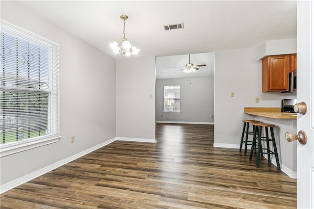 interior space featuring a breakfast bar, baseboards, brown cabinets, dark wood finished floors, and pendant lighting