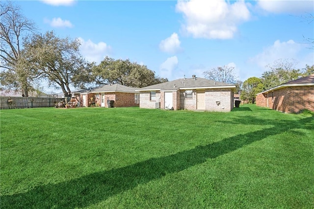 rear view of property with brick siding, fence, and a yard