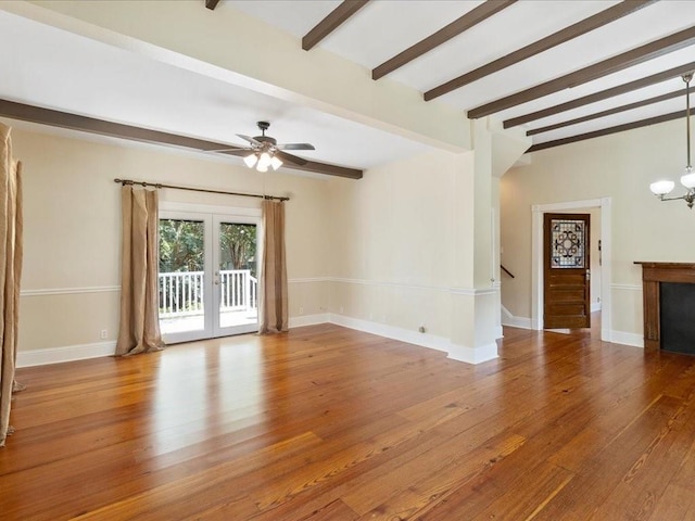 unfurnished living room featuring baseboards, stairway, wood finished floors, beamed ceiling, and ceiling fan with notable chandelier