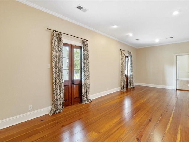 spare room featuring light wood finished floors, baseboards, visible vents, and ornamental molding