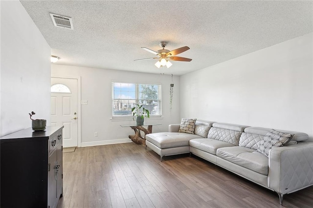 living room featuring ceiling fan, a textured ceiling, wood finished floors, visible vents, and baseboards