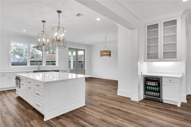 kitchen featuring light countertops, ornamental molding, dark wood-type flooring, white cabinetry, and beverage cooler