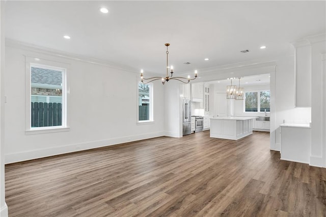 unfurnished living room featuring ornamental molding, recessed lighting, a notable chandelier, and wood finished floors