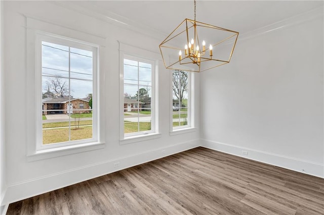 unfurnished dining area with crown molding, baseboards, a chandelier, and wood finished floors