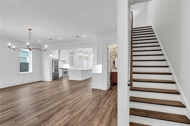 unfurnished living room featuring ornamental molding, a notable chandelier, stairway, and wood finished floors