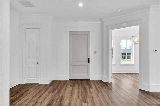 foyer entrance with crown molding, visible vents, wood finished floors, a chandelier, and baseboards