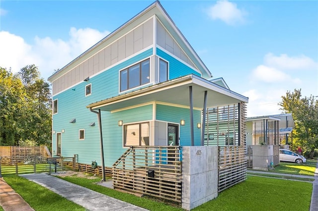 view of front of home with covered porch, board and batten siding, a front yard, and fence